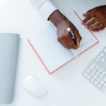 Person Writing on White Paper Beside Apple Magic Mouse