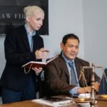 Ethnic male lawyer showing document on laptop to young female colleague